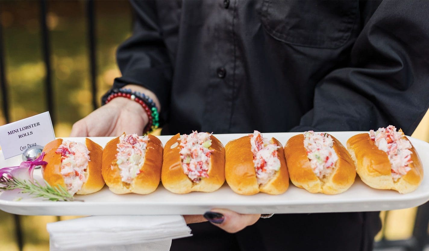 Server in black shirt holds a white tray of mini lobster rolls, with a "Mini Lobster Rolls" card on the left.